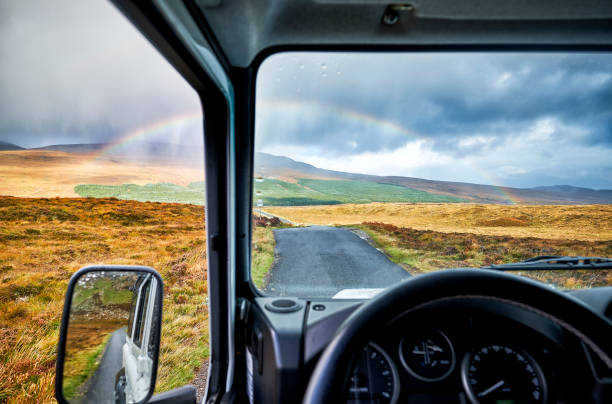 A rainbow over the landscape in scotland seen from a 4x4 car along the route of the north coast 500. The road leads through the landscape.