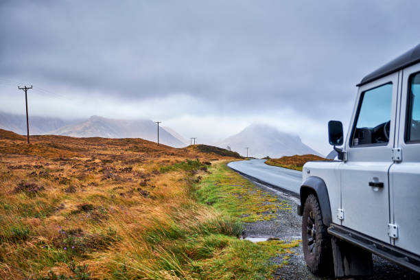 A 4x4 parked along a path during a road trip in Scotland. In the background we see a road and the mountains. It is a cloudy day on isle of skye