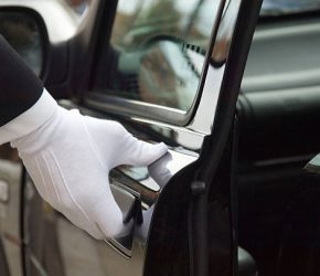 The white gloved hand of a uniformed doorman / chauffeur opening / closing a black car door.